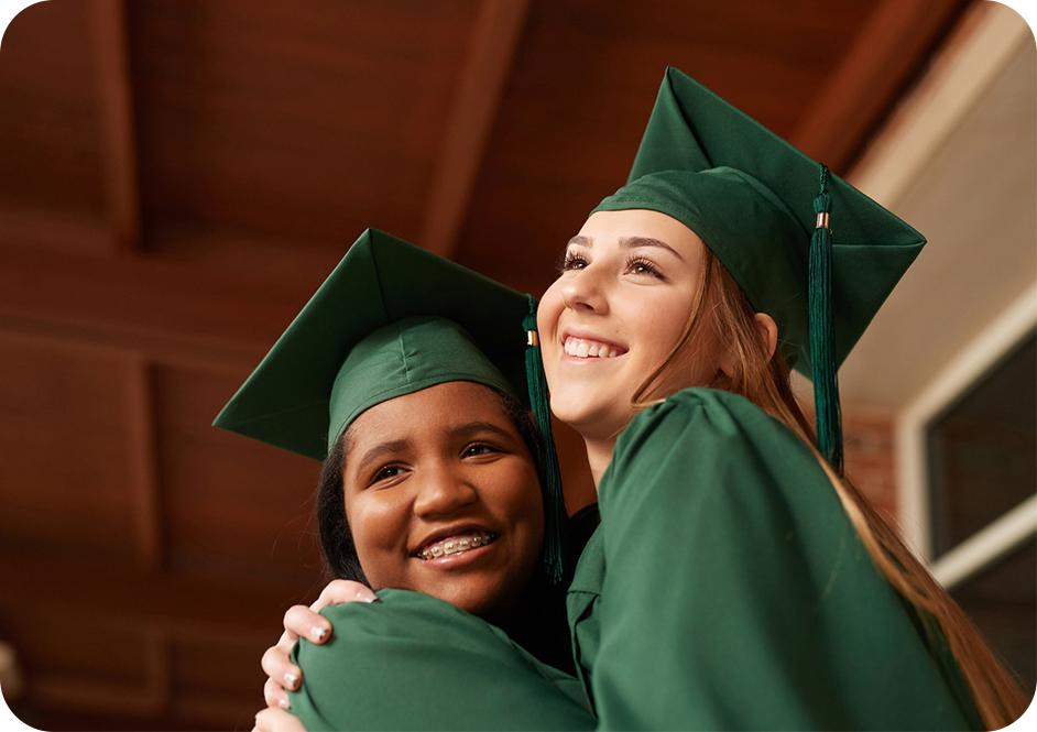 Two girls hugging while wearing green graduation caps and robes
