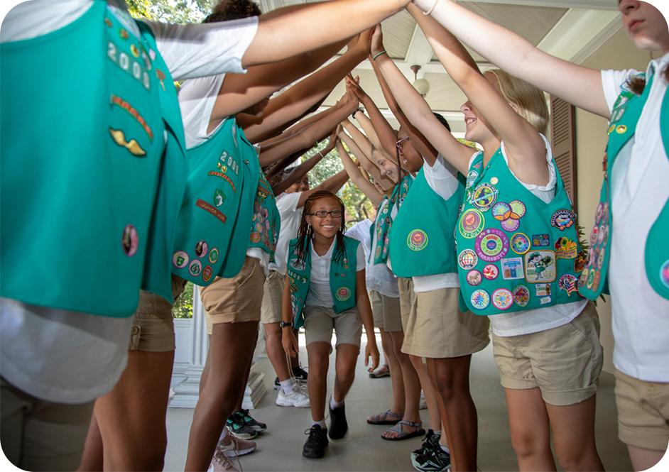 Girl walking through arch made of other girls holding hands while wearing green Junior Girl Scouts uniforms