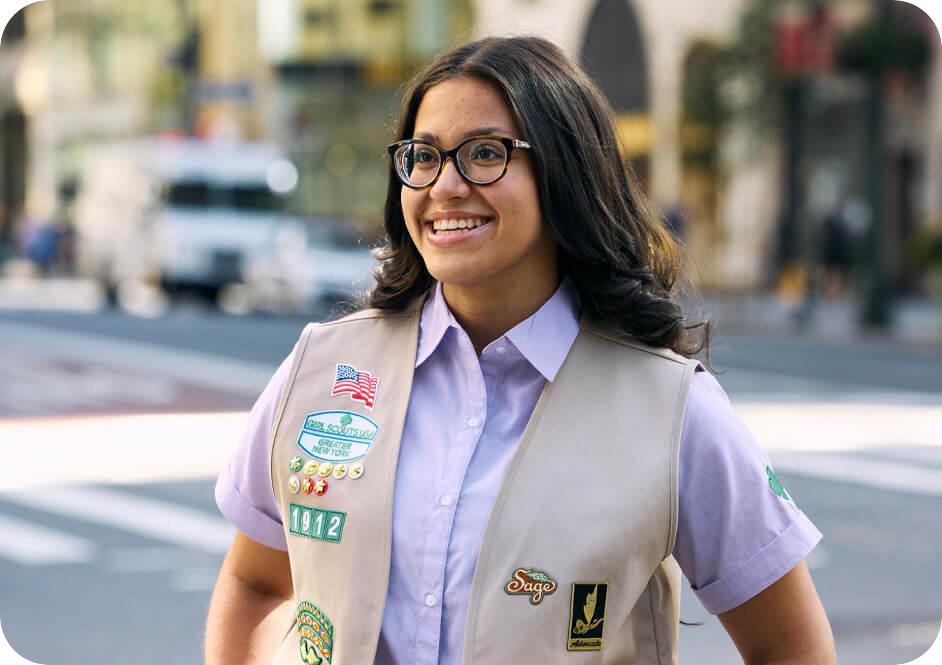 Girl wearing light blue button down short sleeve shirt and tan Girl Scouts uniform vest