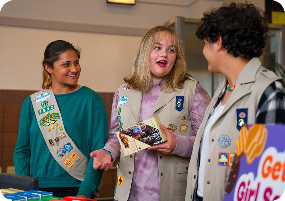 Three girls wearing tan Girl Scouts uniforms and selling Girl scouts cookies
