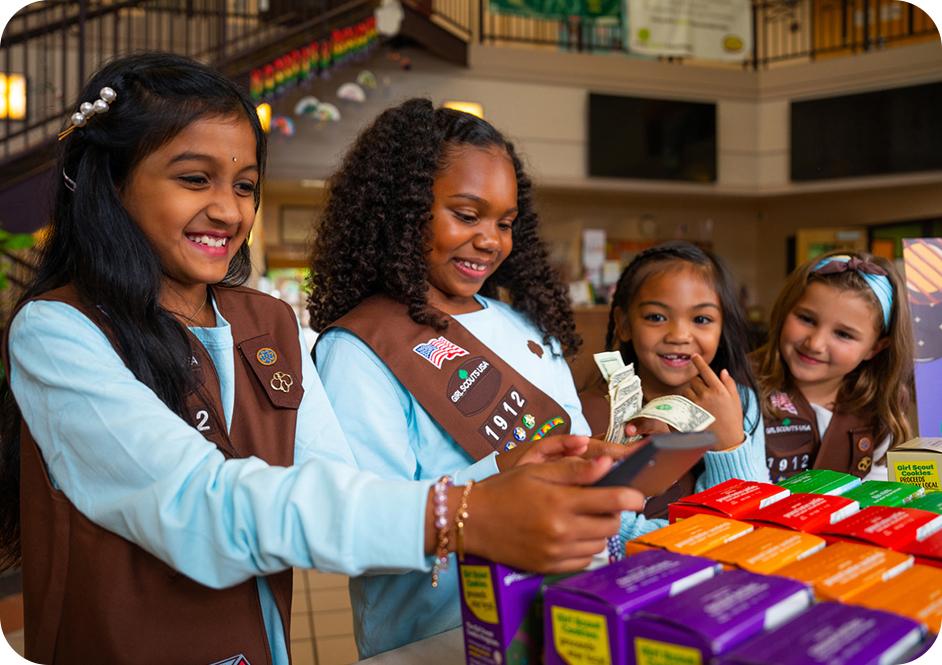 Four girls in Brownie Girl Scout uniforms selling cookies