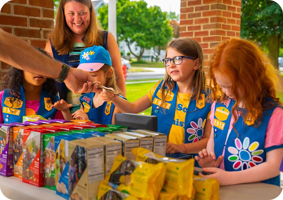 Four girls selling Girl Scout cookies at a booth
