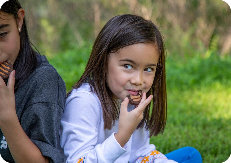 Girl in light purple long sleeve shirt eating a chocolate cookie