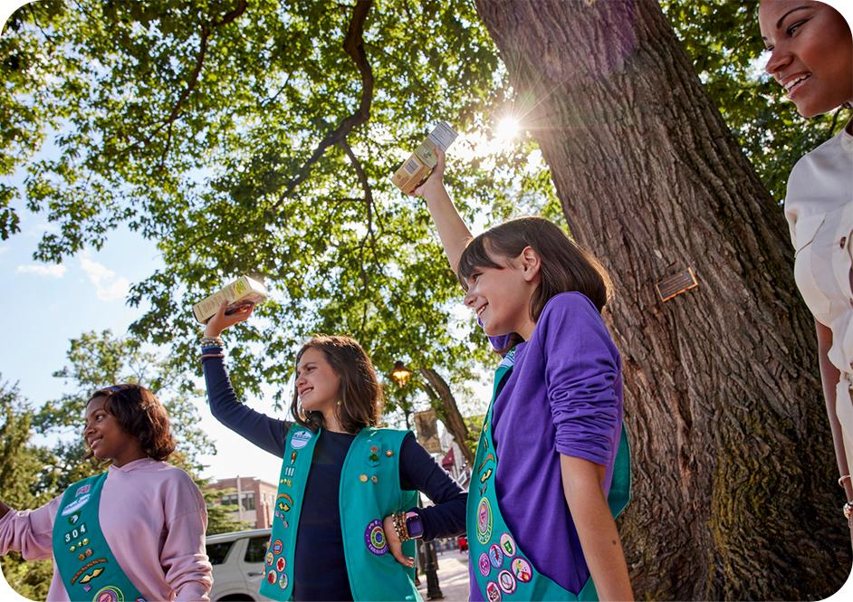 Four girls wearing green Junior Girl Scouts uniforms and holding Girl Scout cookie boxes