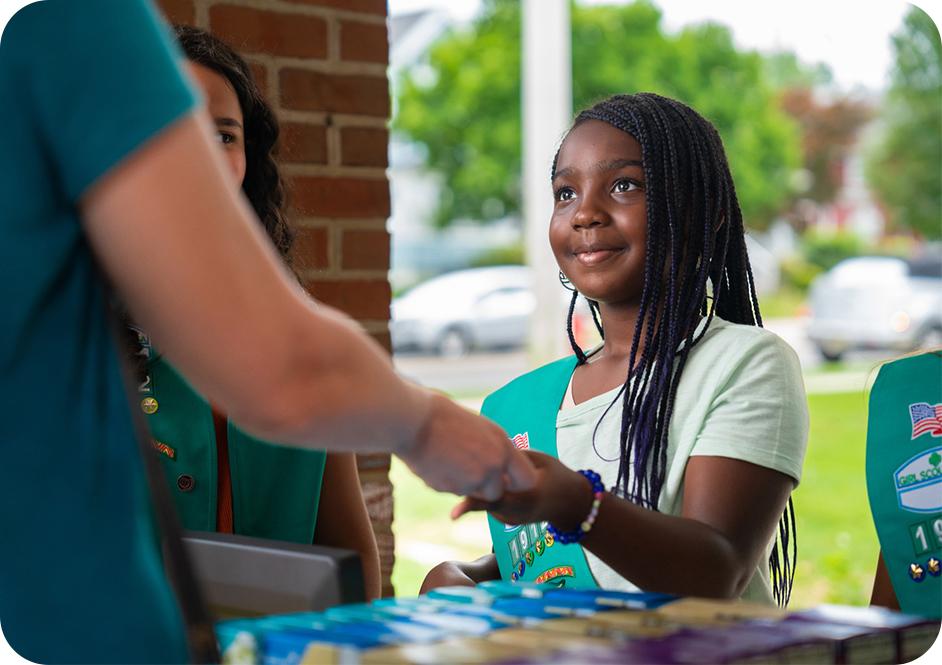 Girl wearing green Junior Girl Scouts uniform sash while selling Girl Scouts cookies