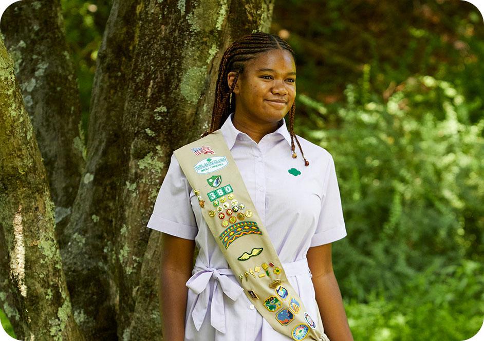 Girl wearing light purple button down short sleeve dress and tan Girl Scouts uniform sash