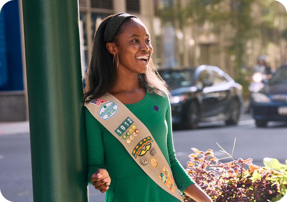 Girl wearing green long sleeve dress and tan Girl Scouts uniform sash