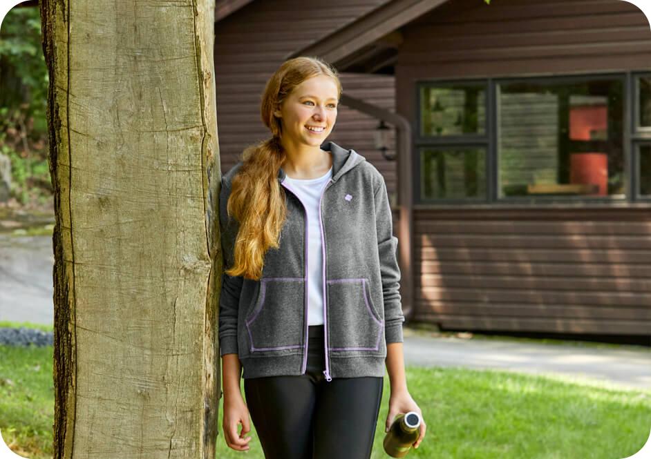 Girl wearing grey Girl Scouts hooded sweatshirt leaning on tree