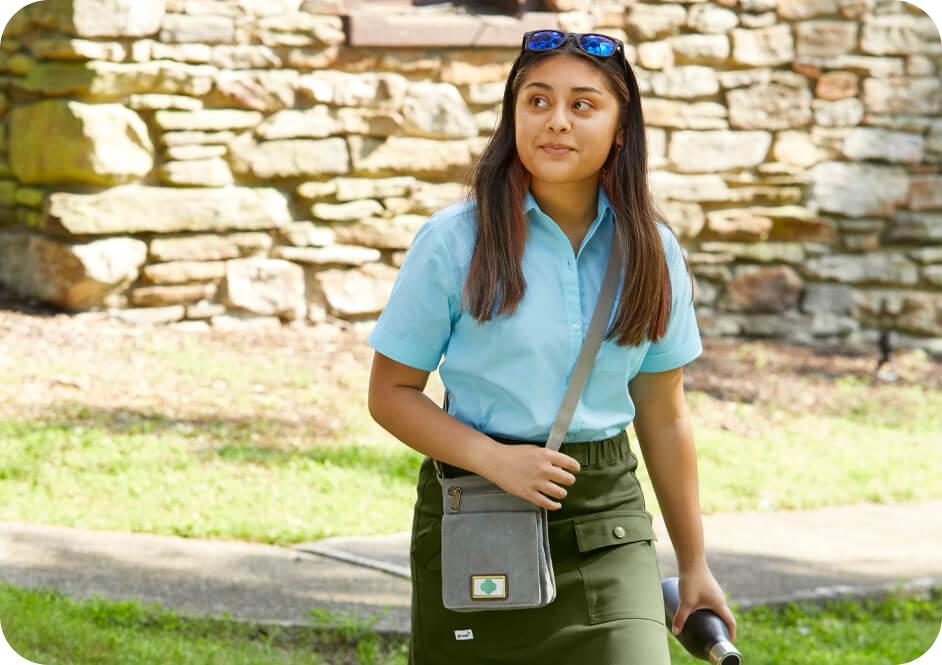 Girl wearing light blue short sleeve button down shirt, green skirt, and grey crossbody purse