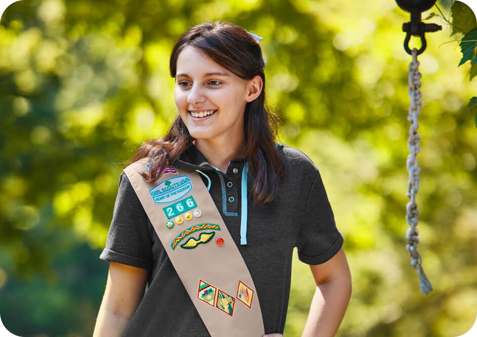 Girl wearing dark grey shirt and tan Girl Scouts uniform sash