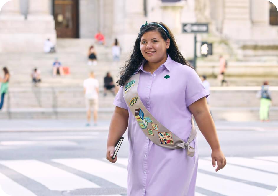 Girl wearing light purple button down dress and tan Girl Scouts uniform sash