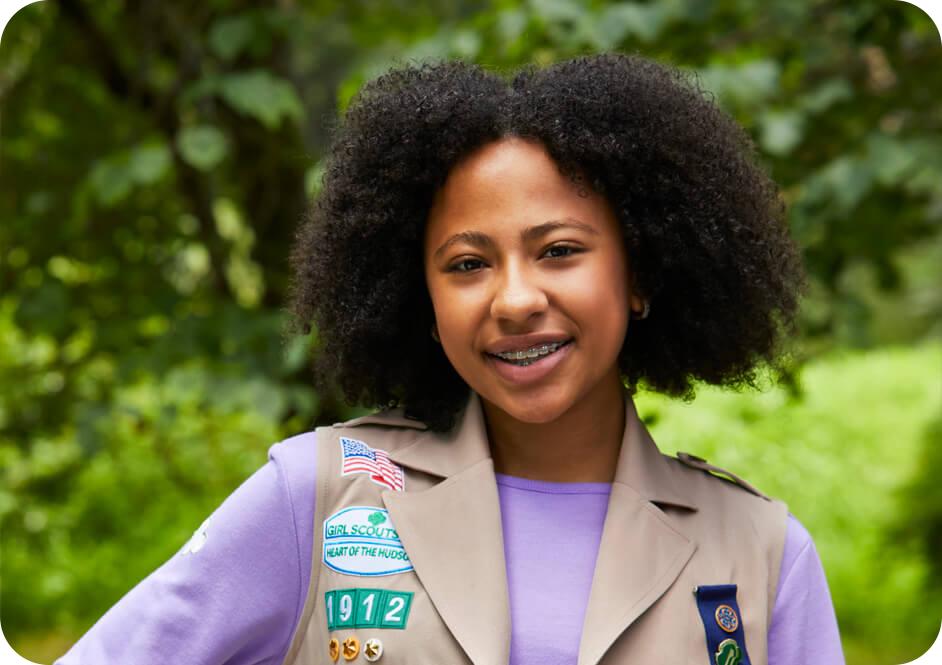 Girl wearing light purple long sleeve shirt and tan Girl Scouts vest