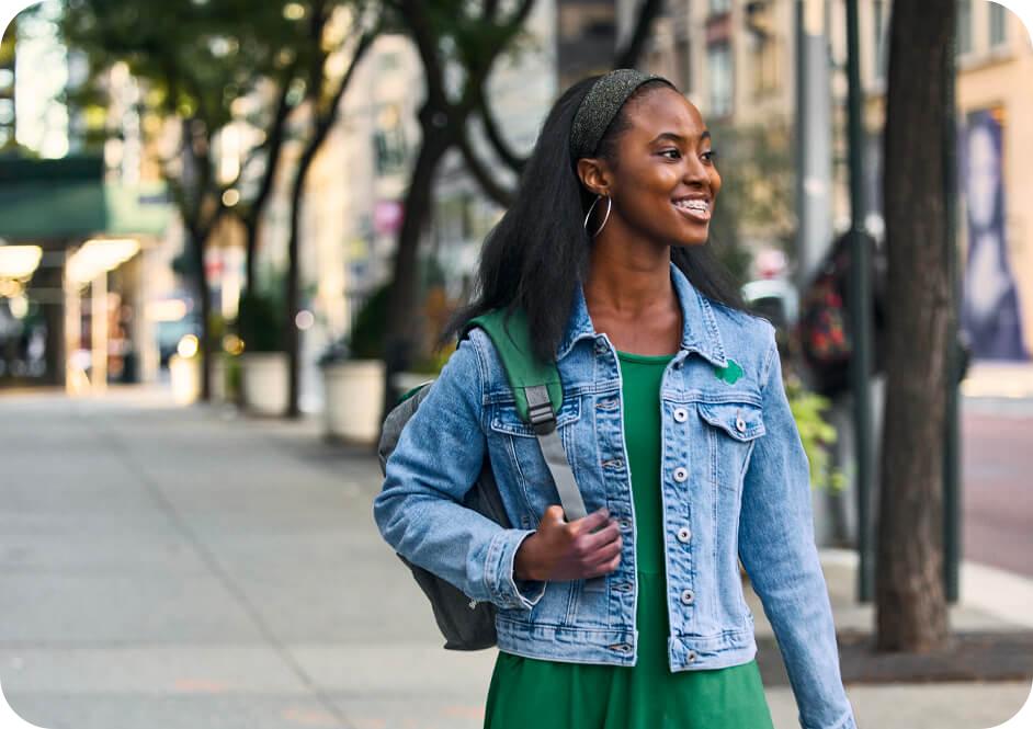 Girl wearing green dress, blue denim Girl Scout jacket and carrying backpack