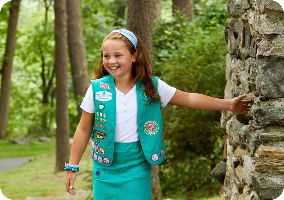 Girl wearing green Girl Scout vest, white t shirt, and green skirt