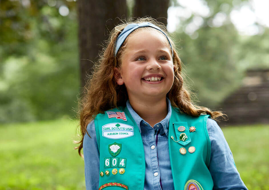 Smiling girl wearing green Girl Scout uniform vest and blue button down shirt